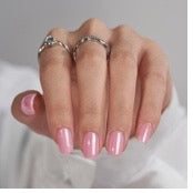 Close-up of a hand with pink nail polish and silver rings on a white background